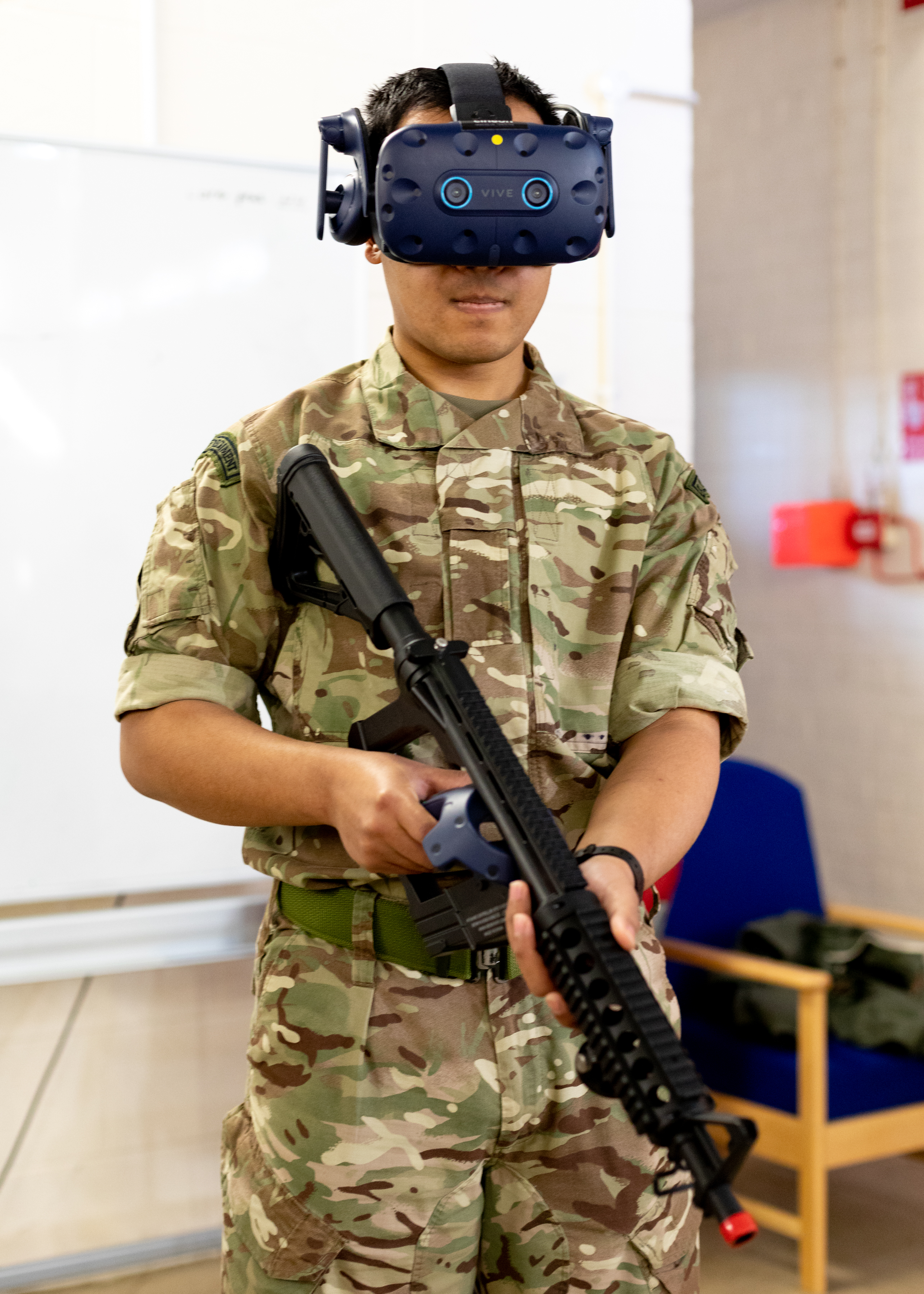 Personnel holds rifle while wearing virtual reality headset.